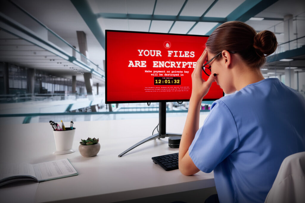A stressed healthcare worker in a hospital setting looks at a computer with a red screen warning that files are encrypted by ransomware.
