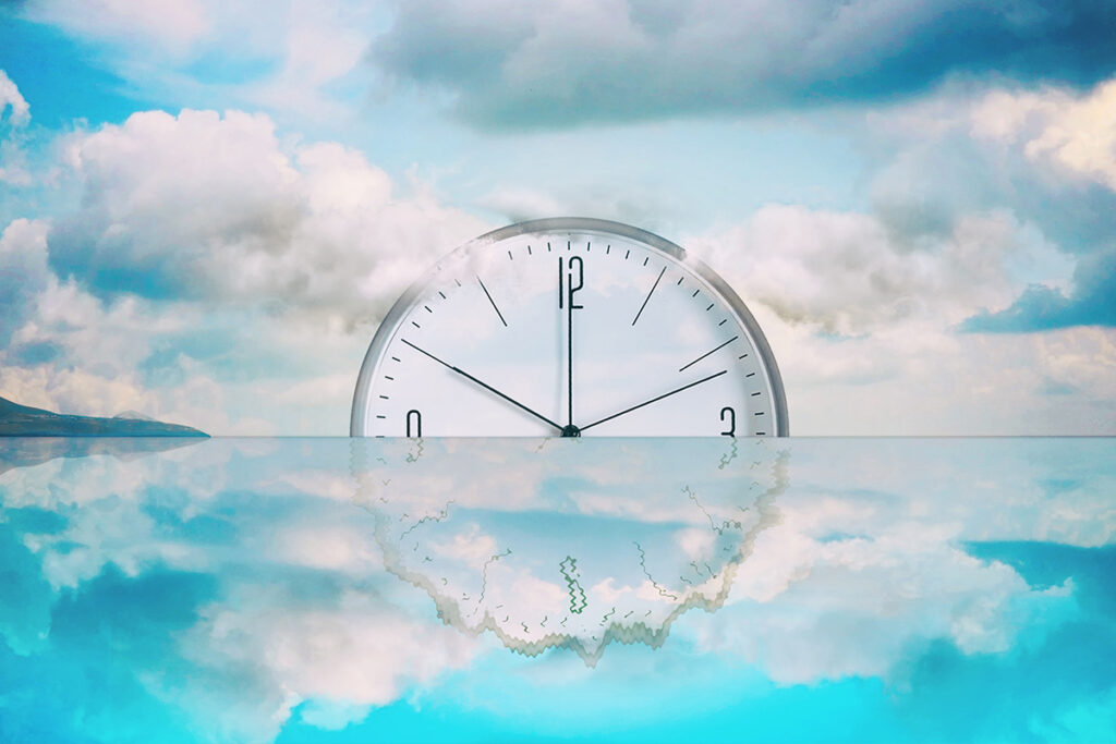 A surreal landscape featuring the top half of a large, white analog clock emerging from calm, reflective water under a cloudy blue sky. The clock's reflection in the water is warped and distorted.