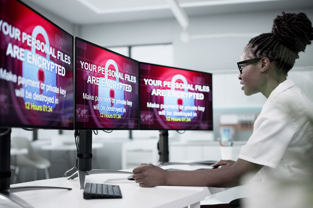 A female IT professional responds to a ransomware attack. Her three computer monitors display an encryption alert and a ransom demand countdown.
